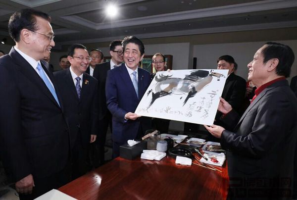 故宫文创展上，众人围绕纯本森活画案正在欣赏北京奥运会吉祥物福娃设计者韩美林（右一）画作